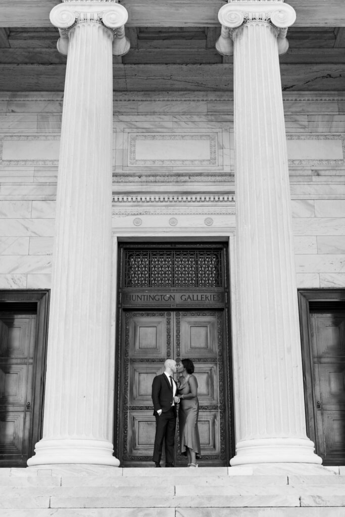 husband and wife kiss one another during their engagement session, outside of the entrance of The Cleveland Museum of Art in Cleveland Ohio. Photo taken by Cleveland wedding photographer Aaron Aldhizer